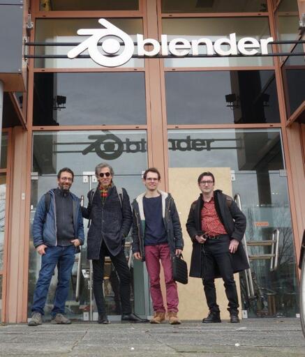 4 people in front of a metal and glass door outside of the Blender foundation with the Blender logo in white at the top. 